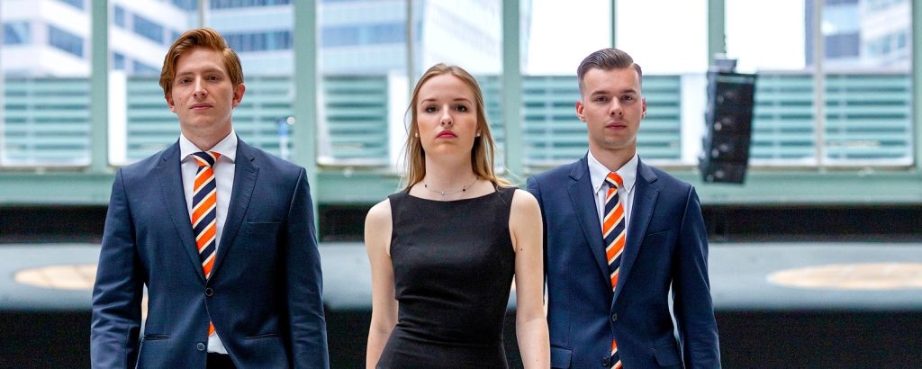 Drie zelfverzekerde studenten van EuroCollege in zakelijke outfit, lopend in een moderne, stedelijke omgeving – symbool voor ambitie en professionele mindset.